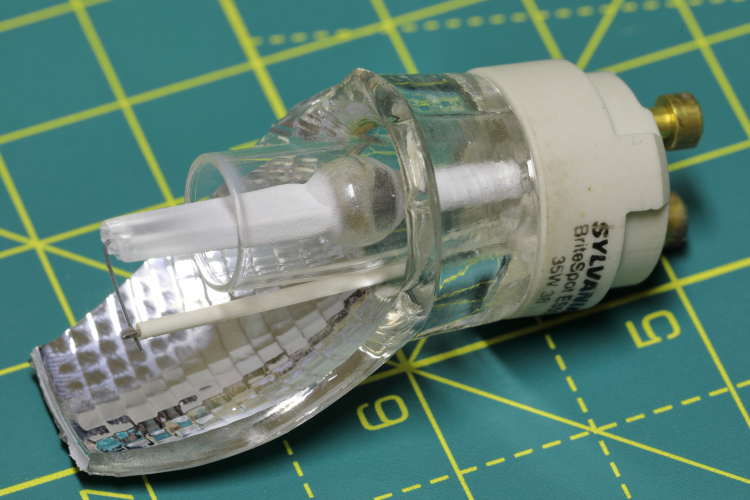 Sylvania BriteSpot ES50 35w MR16 Quartz Metal-Halide: Arc Tube
ne of these tiny little MR16 metal halide lamps which I have was EOL so I decided to have a look inside.

You can see the tiny pea sized arc tube mounted vertically inside a positively charged hard glass sheath. This is to increase colour stability during it's lifetime by preventing sodium loss. The lead wire is also sheathed for this reason.

To maintain a good thermal balance inside the lamp which is critical to prevent oxidation of the molybdenum foil of the arc tube seals the lens end of the seal is made longer to keep it cooler while the cap at the other end acts as a heat sink.
