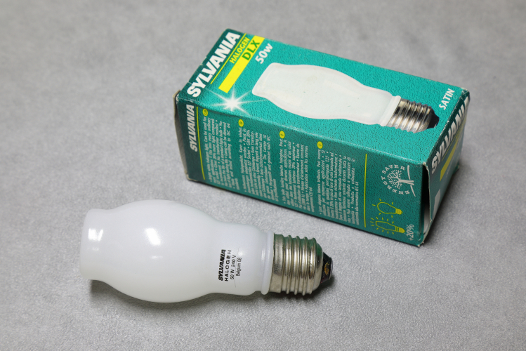 Sylvania 50w DLX Hard Glass Halogen Capsule: Satin
1 x Sylvania 50w DLX double-jacketed tungsten halogen lamp with an aluminosilicate hard glass capsule instead of the more usual quartz which is quite unusual for a European lamp.

The advantages of a hard glass capsule is that it is cheaper and easier to work with as it's melting point is a lot lower than quartz.

The disadvantages are that they can explode quite energetically when they reach end of life which has to be taken into account.
In this case protection is provided in the form of a very impressively thick and heavy outer envelope which is quite something when you have the lamp in your hand!
In fact the outer envelope was made by a Belgian manufacturer of perfume bottles and you can really see the lineage!
This example has a satin diffused finish which has a rough texture when felt.

