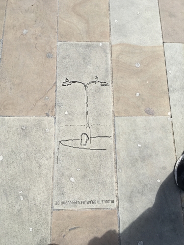 Streetlight street art.
There is a large pedestrianised area at the front of Liverpool Lime St railway station that was refurbished a few years ago. 

Scattered about are these strange engravings in the paving slabs and I never really paid much attention to them until one day I spotted this one, and immediately recognised what and where it was in real life.

At the pier head near the cruise terminal there is an old quay with several old concrete columns with derelict G.E.C Z8420 lanterns on them. What makes them interesting is that there is usually one or two Cormorants perched on the outreach arms drying their wings after a fishing session. 
Looks like Iâ€™m not the only one to notice this as the birds and lanterns are in this strange bit of street art....

The real lanterns and bollard (no birds sadly) can be seen here:
[url]http://80.229.24.59:9232/gallery/displayimage.php?pid=6560[/url]
