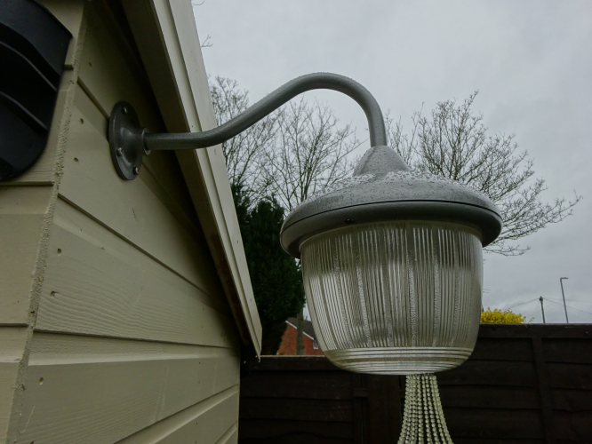 Coughtrie PW15 Installed closeup
This Coughtrie PW15 entered the collection in 2019 iirc, arriving in a well used, but overall good condition, a shocker considering these only have to be exposed to the slightest bit of damp and the screws seize solid. Upon arrival, it ran 125w MBF. I removed that and put it back to 2 pin BC, but from there it just ended up in storage in my lanterns shed, getting a bit battered from poor storage.

It was very much a spur of the moment decision to strip down and restore it, mainly due to the fact I really like it and it was becoming criminal that I wasn't doing anything with it.

Over the course of 2 weeks I stripped it down, which was a surprisingly easy task since the screws seize the minute they're screwed tight. I carefully removed any corrosion and drilled out any screws where needed, before spraying the bracket and the exterior of the light hammered grey, the insides going white as they should be. Sealing the glass back into place with silicone sealant proved to be an initially really messy, but overall satisfying job, and leaving the sealant overnight to cure resulted in a perfectly sealed light once again.

Then came installation, and since it wasn't screwing to any battens on the small lamp shed, I drilled though the wood and screwed some machine bolts through, before bolting them in place with a large penny washers to hopefully help spread load. The hardest part about the whole job was actually wiring it in, but once all was done and I switched the outdoor switch on, seeing both come to life was another sure sign of a successful job.

Ironically the lamp shed is the newest of the four sheds I have, yet is now the second shed to have a complete electrical installation!
