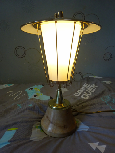 Falks GLS Pedestal light, after restoration and lit.
Earlier this year I bought in this gorgeous Falks Pedestal light, which had been crudely 'upcycled' into a table lamp. Seeing past the mess to the potential it hid beneath the paint and dirt, I bought it and begun looking around for the parts that had been replaced or was missing.
 
First up was replacing the three hex nuts that should have been ball nuts. I managed to find some on eBay in an M4 thread, however they needed to be 4BA thread. I drilled the original thread out, retapped to M5, threadlocked the brass bolt in place, cut it flush and then drilled and tapped to 4BA. Part one done, the next and more complicated part was to find an original finial.

For this I needed to find a photo of one, and thanks to a fellow collector, was show an image of how it should look. This left me needing a piece of brass to turn and reshape, and that ended up showing itself in the most unusual of circumstances. Whilst digging around a column to move it while at work, a team mate hit some metal. It turned out to be an old brass lever, but with the almost perfect dimensions to become a new finial. I got it home, cut most of the bar off to allow me to put it in a drill. I cable tied the drill so it'd constantly spin, and with Dads help and his trusty flap disc in the angle grinder, turned the lever till it matched what I needed. I then cut the bar off completely before drilling and tapping into the now finial to 5/8" BSW. I got a brass bolt, washer and a rubber seal, and screwed the finial into place, really finishing off its 50's style beautifully. So that's the light completed again, the real restoration can now begin.

Polishing the light was actually fairly simple, the black paint on the base chipped off, and the 9 uprights were given to a neighbour to polish since he has a polishing wheel. Once the lid was polished, I painted the inside white, really smartening the whole thing up.
After much debating, I decided to keep it as a table lamp, its too nice to put outside again imo. So the wooden base was given to a mates stepfather, and he turned it with his lathe into a more fluted design, allowing the base of the pedestal to sit over the wood and not in it. It was finished with a light coloured wax to compliment the brass of the now fully polished light. Screwed back to the wood with 4 brass screws, the light was reassembled and rewired with gold flex, a much better fit than the black flex it was wired with.

Honestly I think this has turned out better than I thought it would, and the opal glass really softens the light from whatever lamps inside it (currently a CFL) so this may end up becoming my bedside table lamp.
