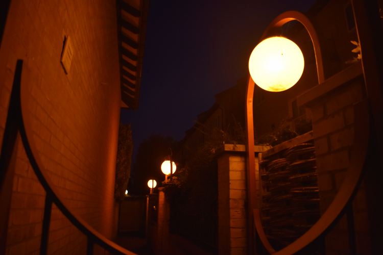 Unusual SON globe lantern installation
Here is a very curious installation I'd been meaning to get a photo of for some time. Lighting a narrow path between the back of some private flats (presumably built in the late '80s to early '90s given the styling of the lanterns and architecture) are these SON globe lanterns built in to the fence/scrollwork. I've never seen anything quite like it!
