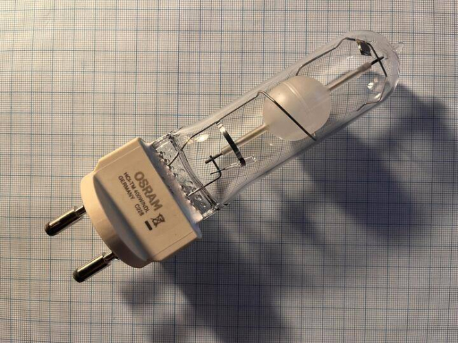 The CDM-T lamp in a T-19 shape undoubtably become for long time one of the most popular lamps used in accent lighting in shops. They were widely used especially in shops selling clothing and other consumer products. Du to the high CRI and color stability as well as a long life these lamps also become very popular for architectural application, like the the immolation of historic building like churches.
Also these lamps were widely used in small fair stands.


However these lamps had one drawback. They were limited to a Power rating of 150W. For buildings were a lots of illumination is needed therefor a compact source quartz metal halide lamp was used. For example the Osram promoted its HTI Lok-It lamps intended for moving-head projectors as the lamps used to illuminate the Brandenburg Gate in Germanys capital city Berlin. However the Life if these lamp is with an average of 750-2000hrs regarding the exact type rather short for a discharge lamp.
Large companies like Siemens, Volkswagen or BMW also looked for a lamp to use at their big stands like the Hannover Messer or the IAA.
By that time Osram already offered larger HCI lamps, the HCI-TS 250W and the HCI-TS 400W. However these seemed to be unpopular.
Osram deamed the demand for these lamps high enough to develop a new lamp range. It would become known as the HCI-TM for the 250W and 400W variety and the HQI-TM for the 600W and 1kW variety. All these lamps were fired in the same physical size The physical size is actually different however all lamps have the same light centre. Allowing a fixture design for all 4 wattages.
The lamps were equipped with an G22 base a GY22 base was in development. The latter would have allowed instand reignition when hot using a 25kV ignitor. If it was ever launched is unknown, however likely it wasn't
The lamps were, similarly to Osram’s other ranges of CMH lamps offered in a in three light colors, 3000K (WDL) 4200K (NDL) and 5900K (D).
The lamps were made at the Radium Factory in Wipperfürth Germany, that at the time also manufactured Osram high power metal halide lamps (HQI-T and HQI-TS 1000W and 2000W) but als some of their HMI lamp.
It seem like the lamps were launched somewhere around 2008. Osram planed to launch an electronic ballast by 2013 for the HCI-TM lamps. Until then it was recommended to run them on normal high pressure sodium chokes (230V mains for the 600W and 1kW variety). I do not know if these ballast ever came and it is believed that these Lamps were never a huge success and failed replacing traditional optical MH lamps from the applications listed above. While the exact date is unknown it is believed that these lamps were discontinued around 2015. 
Philips however also developped a 250W CDM lamp comparable to the smaller version of this lamp. However philips used a standard G12 base. Wile the G12 base is not capable to isolate the 25kV present at hot restrique, it allows to use lamps very similar to the stadard CDM series. This is however not possible with the bigger 400W Lamp. 
This particular lamp was made in 2012 and already feature as small UV source as starting aid to substitute the Radioactive Kr85 which was omitted due safety regulations.
It uses a classic Osram discharge vessel made from two half spheres of ceramic welded together in the middle. The resulting seem may be seen if the picture is enlarged.
This two part designed simplified manufacturing, reduced the mass of the discharge tube and improved color stability over the lamps life. Osram was the first lamp manufacturer employing this technology. It become standard for Osram CMH lamp by the early 2000s.
Also notable is the coiled lead in wire for the top electrode. This prevents shadows. It also maked the forces from the magnetic field of said wire on the plasma more uniform. 
